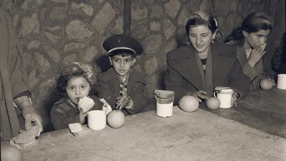 Children newly arrived from Iraq at a reception table with bread, oranges and mugs, 1951.