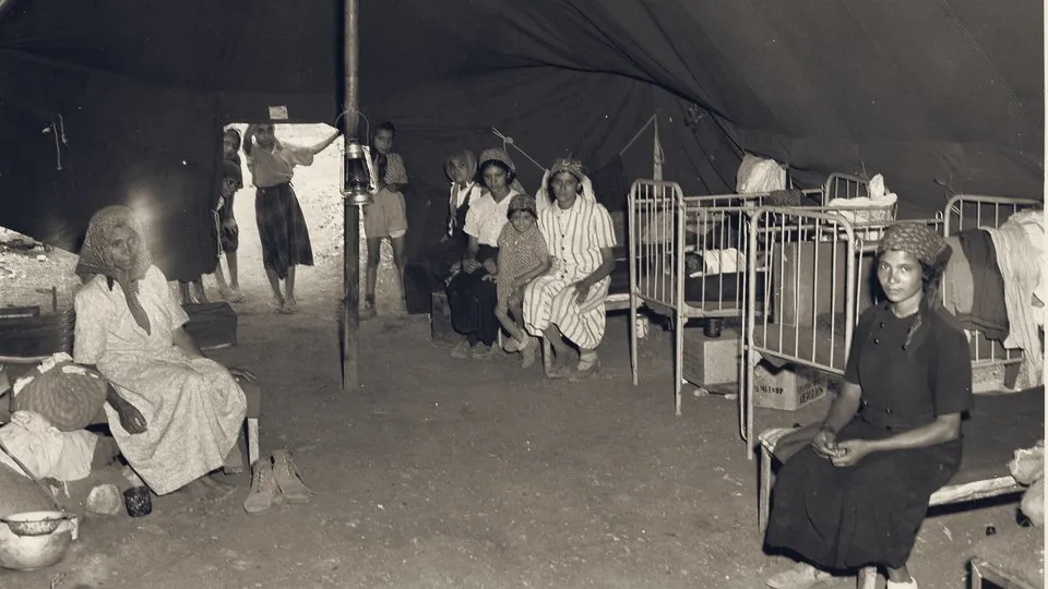 Immigrant women and children inside a large tent at a ma'abara on the road to Jerusalem, 1950.
