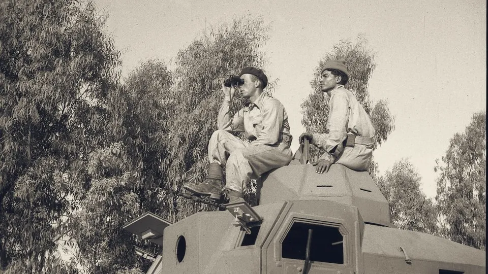 Two soldiers keep watch from an armoured car among eucalyptus trees during the capture of Lydda airport, 10 July 1948.